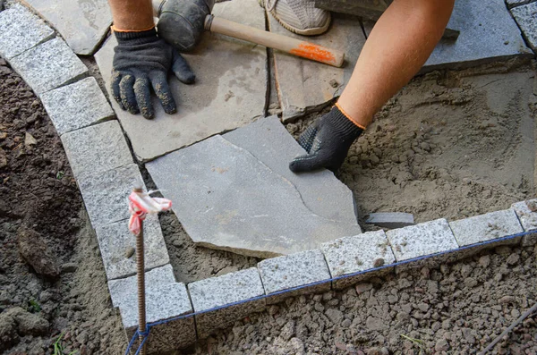 Evin yakınında asfalt inşaatı. Tuğlacı kaldırım inşaatı için beton kaldırım taşı blokları yerleştirdi
