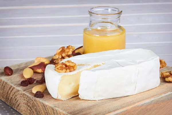 Сыр с орехами на деревянном лотке и белом столе — стоковое фото