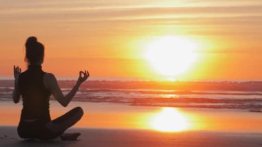 Gün batımında kumsalda ince kadın silueti, yoga pratiği.