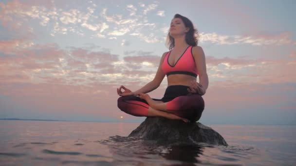 Genç bir kadın gün batımında nilüfer çiçeği pozisyonunda meditasyon yapıyor. — Stok video