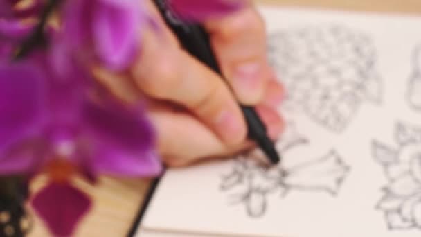 Artiste féminine dessine une fleur dans un style rustique, un carnet de croquis sur une table — Video