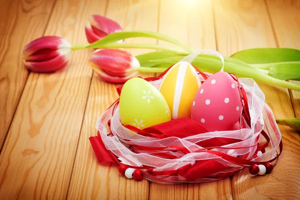 Oeufs de Pâques colorés sur fond en bois avec des tulipes — Photo