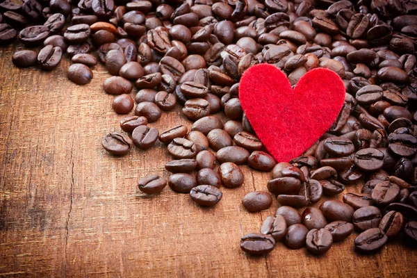 Coração vermelho e grãos de café no fundo de madeira — Fotografia de Stock