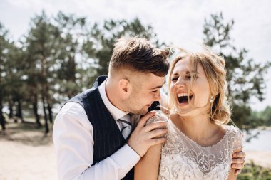 Mutlu gülümseyen düğün çifti. Güzel gelin ve şık damat, nehrin ve ormanın arka planında gülüyor..