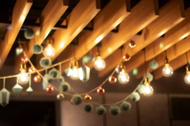 Bulanık arkaplan, doku. Noel ve yeni yıl için lambalardan ve Noel oyuncaklarından dekorasyon. Eski lambaların ve kağıt figürlerin altın bulanık çelenkleri ahşap kirişlerin tavanından sarkıyor. Metin için yer