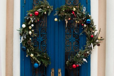 Açılış demirhanesi olan mavi eski bir kapının üzerindeki Noel ağacından büyük bir çelenk. Evin girişinin şenlikli dekorunda kocaman bir çelenk, parlak Noel oyuncakları ve kurdeleler var. Noel havası