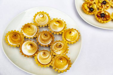 Beyaz tabakta krema ve kremalı iştah açıcı kurabiyeler, ziyafet masası. Açık büfede gözleme. Düğündeki misafirler için çikolata. Tartlet şeklinde pasta. Krem çiçeklerle süslenmiş pasta.