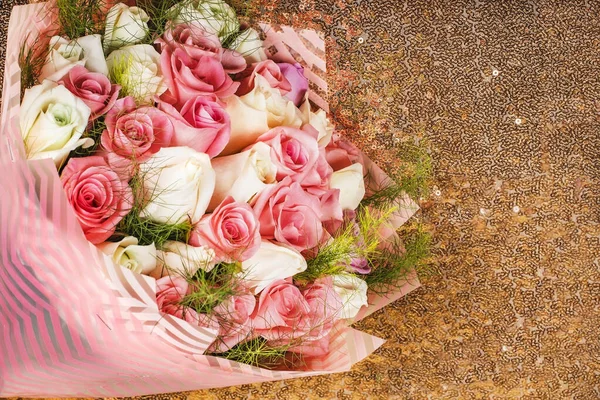 A large bouquet of delicate roses of pastel flowers lies on a gold background. Bouquet as a gift for the holiday or wedding. Flower arrangement for holiday decoration. Place for text