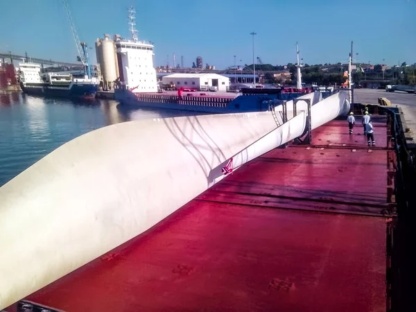 The large blades of the wind farm are fixed on the deck of the ship in the port. Transporting the blades of the wind farm to the installation site on the ship.