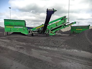 Mekanize yük yüklemesi. İskelede çakıl yığınları ve taşıma kemeri olan bir hasat makinesi. Bir hasat gemisi teslimat için bir denizaşırı gemiye kömür yüklüyor.