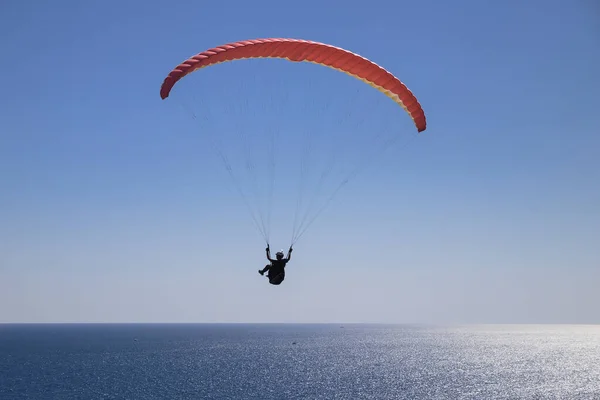 A brave man is flying on a paraglider over the open sea on a bright, sunny day. Tourist attraction in the seaside resort.