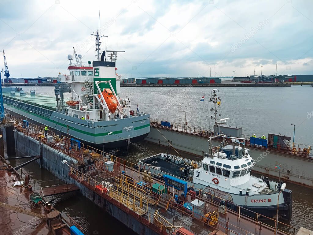 07.31.2021 Netherlands, Delfdzijl A tug pulls a dry cargo ship to dry dock for repairs at a shipyard. Towing a transport vessel by tug for repair to dry dock at a shipyard. the tug is docking the ship