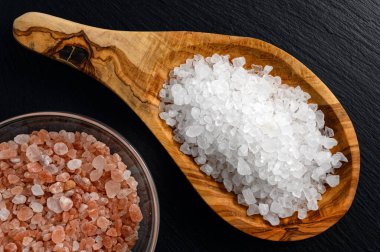 Deniz ve Himalaya tuzu ahşap kaşıkta ve cam kavanozda siyah arka planda.