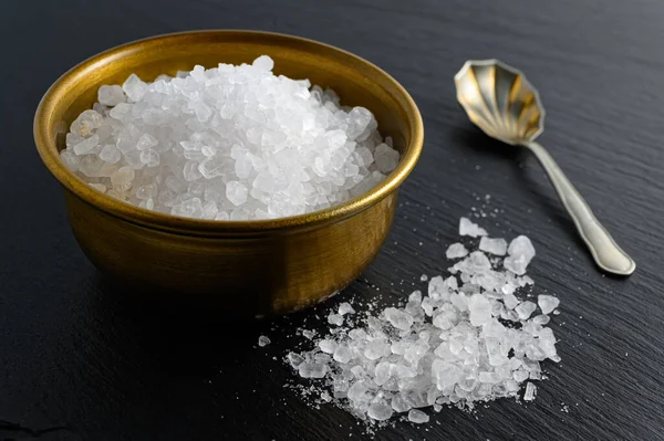 Bronze bowl of sea salt and small spoon on black background