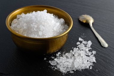 Bronz kase deniz tuzu ve siyah arka planda küçük kaşık. 