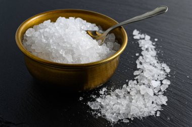 Bronz kase deniz tuzu ve siyah arka planda küçük kaşık. 