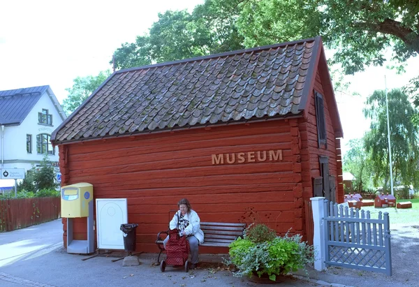 Starsza pani siedzi przed małe muzeum — Zdjęcie stockowe