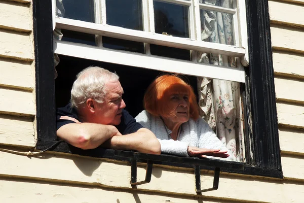 Elderly couple look out from their window — Stock Photo, Image