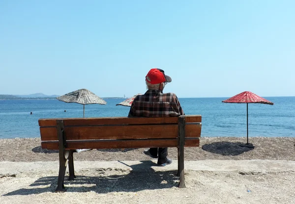 Elderly man sitting on a bench by the beach — Stock Photo, Image