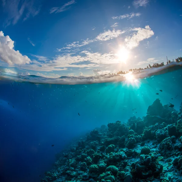 Récif corallien en pleine mer avec surface de l'eau et rayons du soleil. Ciel et nuages au-dessus de l'océan . — Photo