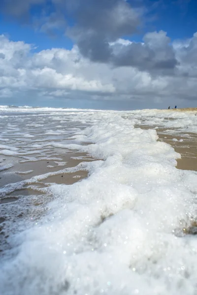 Vítr a vlny tvoří pěnu na pláži — Stock fotografie