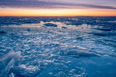 Sahilde kış manzarası, kıyı şeridi çatlamış buz, kar ve gün batımında açık deniz suyu..