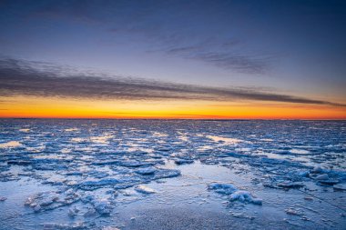Sahilde kış manzarası, kıyı şeridi çatlamış buz, kar ve gün batımında açık deniz suyu..