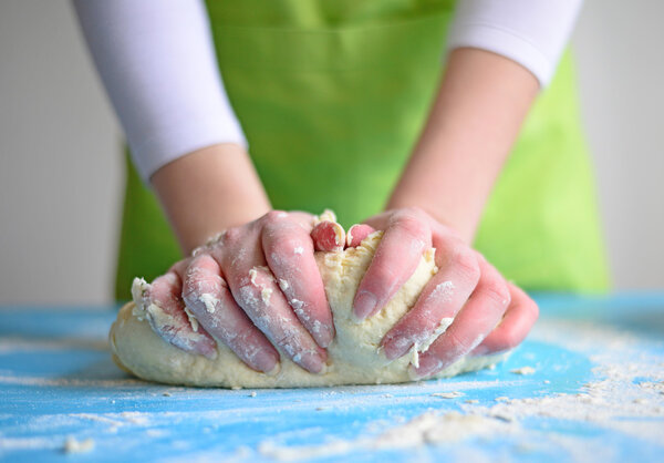 Woman's hands knead dough on a table