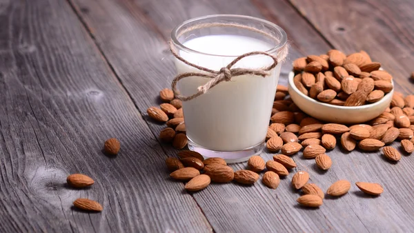 Almond milk in glass with almonds in bowl, on wooden background — Stock Photo, Image