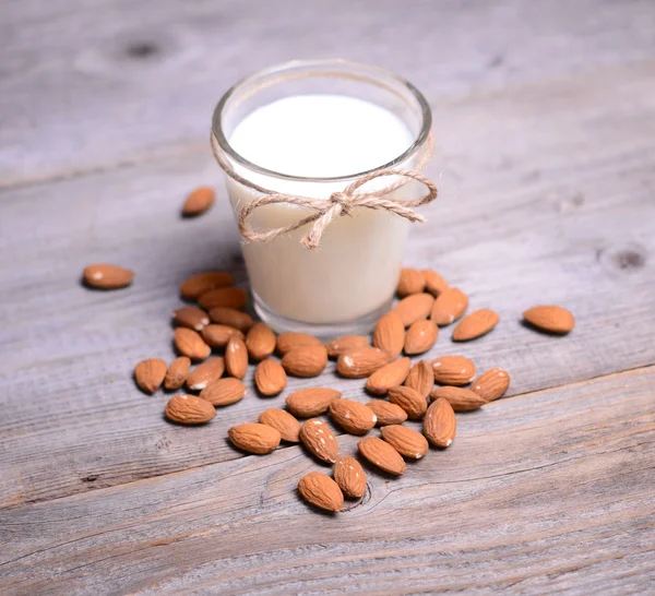 Leche de almendras en vaso con almendras sobre mesa de madera —  Fotos de Stock