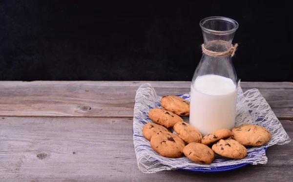 Botella de leche con galletas sobre mesa rústica — Foto de Stock