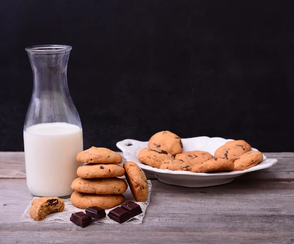 Pila de galletas con chispas de chocolate y botella de leche en pizarra — Foto de Stock
