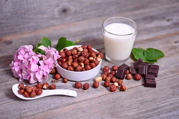 Hazelnut segar, coklat gelap dan segelas susu di atas meja kayu — Stok Foto