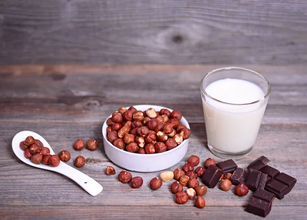 Świeżych orzechów laskowych, ciemnej czekolady i szklankę mleka na drewnianym stole — Zdjęcie stockowe
