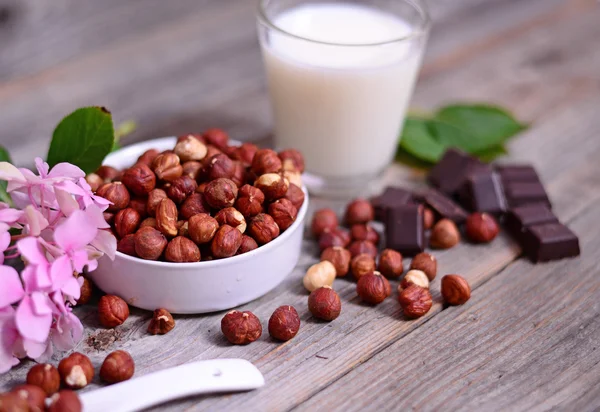 Verse hazelnoot, donkere chocolade en glas melk op houten tafel — Stockfoto