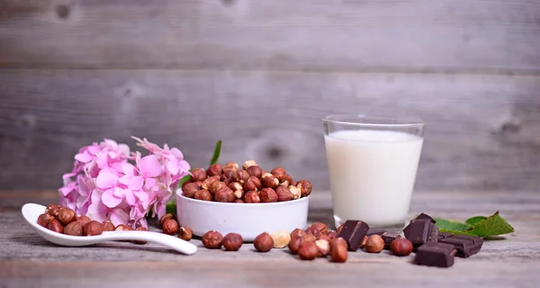 Hazelnut segar, coklat gelap dan segelas susu di atas meja kayu — Stok Foto