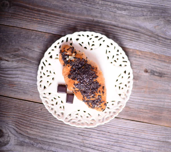 Croissant al cioccolato su piastra bianca su fondo legno — Foto Stock