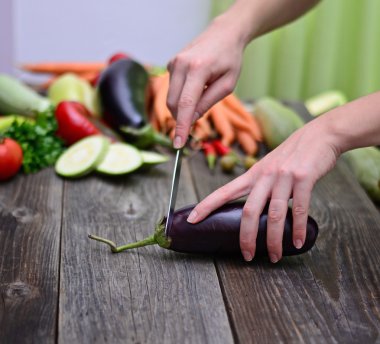 Woman's hand cut fresh eggplant on table clipart