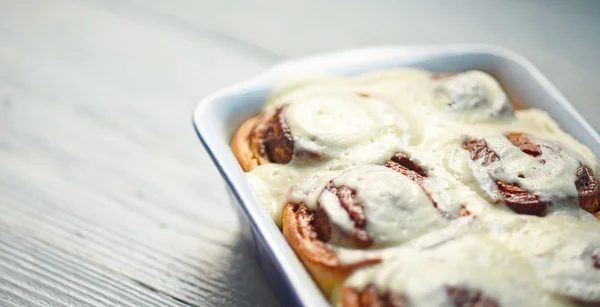 Rouleaux de cannelle dans un plat de cuisson en céramique sur table blanche — Photo