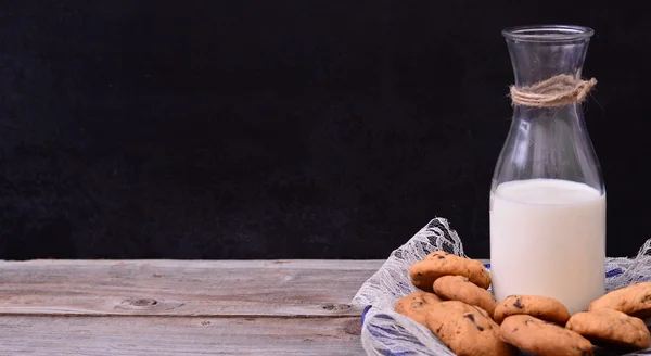 Botella de leche con galletas sobre mesa rústica — Foto de Stock