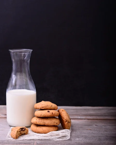 堆栈的巧克力曲奇饼干和瓶牛奶在黑色背景动态 — 图库照片