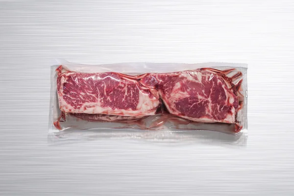 Ongeopende pack 2 rauw rundvlees steaks op een gepolijst aluminium keukentafel, zonder etiket — Stockfoto