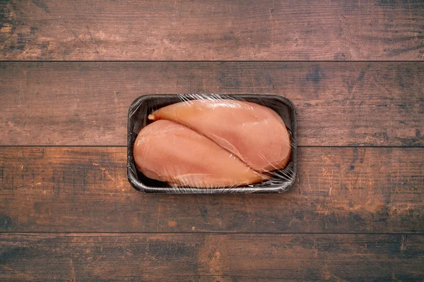 Oöppnad förpackning med 2 rå kycklingfilé på en gamla rustika träbord, utan etikett — Stockfoto