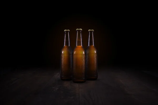 Tre bottiglie di birra in piedi su un tavolo di legno rustico — Foto Stock