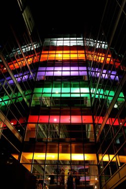 Geceleri renkli ışıklarla aydınlatılmış çok katlı cam bina.