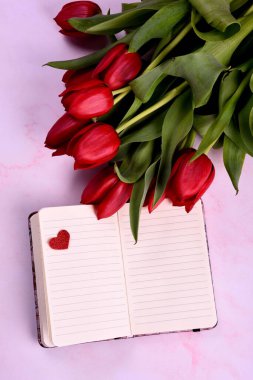 Kırmızı lale buketi, not defteri ve pembe arka planda kırmızı kalpler. Sevgililer günü, kadınlar günü ve anneler günü konsepti. Yukarıdan görüntüle 