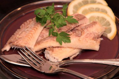 Koyu bir tabakta, limonla süslenmiş balık filetosu. Tuzda pişmiş balık. 