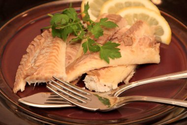 Koyu bir tabakta, limonla süslenmiş balık filetosu. Tuzda pişmiş balık. 
