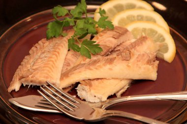 Koyu bir tabakta, limonla süslenmiş balık filetosu. Tuzda pişmiş balık. 