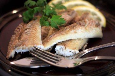 Koyu bir tabakta, limonla süslenmiş balık filetosu. Tuzda pişmiş balık. 